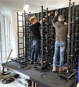 Techniciens assemblant un mur d'écran LED dalle par dalle sur praticables